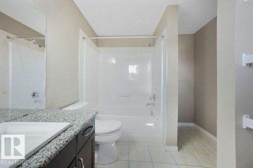 Bathroom featuring a white tub and shower combination with chrome fixtures, a toilet, a vanity with a light-colored speckled countertop and integrated white sink, and dark wood-finish cabinetry with silver hardware - 1306 32A Street, Edmonton, AB 