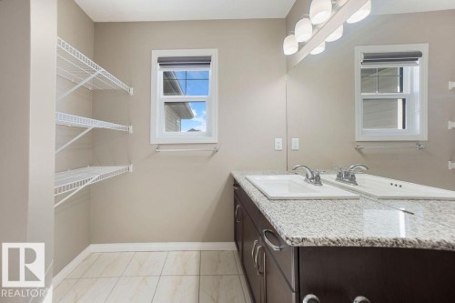 Double vanity with a granite countertop and dual sinks, complemented by a large wall-mounted mirror and overhead lighting fixture - 1306 32A Street, Edmonton, AB 
