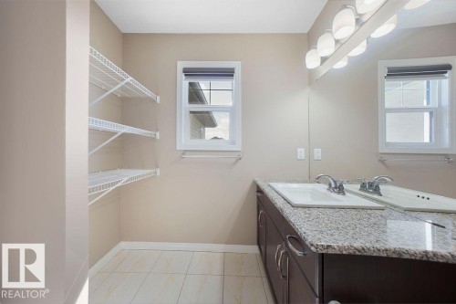 Bathroom featuring a dual sink vanity with a granite-finish countertop, dark wood-finish cabinetry, and contemporary light fixtures - 1306 32A Street, Edmonton, AB 