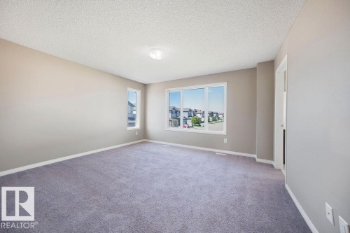 Spacious room featuring neutral wall tones, textured ceiling, light gray carpeting, and multiple windows - 1306 32A Street, Edmonton, AB 