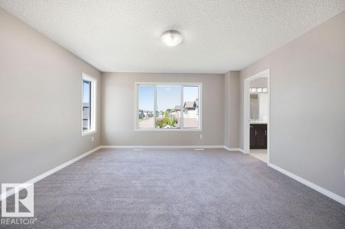 Spacious room featuring neutral carpeting, light gray walls, white trim, and multiple windows - 1306 32A Street, Edmonton, AB 