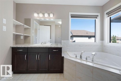 Bathroom featuring a corner soaking tub with tile surround, a dark wood-finish vanity with a light-toned countertop, a rectangular undermount sink, and open shelving - 1306 32A Street, Edmonton, AB 