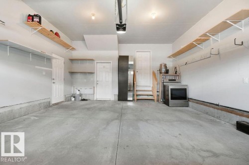 Spacious garage featuring concrete flooring, multiple overhead lighting fixtures, and integrated wall shelving for organized storage - 1306 32A Street, Edmonton, AB 