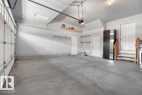 Spacious garage with a concrete floor, overhead lighting, an automatic garage door opener, two side entry doors, and built-in shelving for organization - 1306 32A Street, Edmonton, AB 