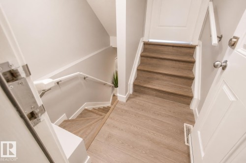 Multi-level interior featuring wood-finish flooring, white baseboards, and a white handrail - 1306 32A Street, Edmonton, AB 