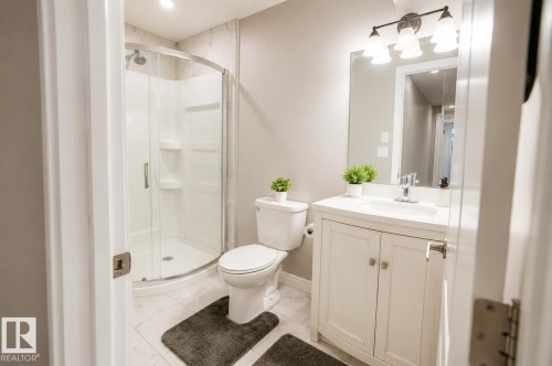 Bathroom featuring a corner shower with glass enclosure, white vanity with integrated sink, chrome faucet, and overhead vanity lighting - 1306 32A Street, Edmonton, AB 