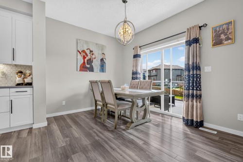 Dining area featuring wood-finish flooring, a contemporary chandelier, and a sliding glass door providing direct access to an outdoor deck - 2534 Wonnacott Loop, Edmonton, AB 