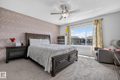 Carpeted room featuring a large window, a ceiling fan with integrated lighting, and a textured accent wall - 2534 Wonnacott Loop, Edmonton, AB 