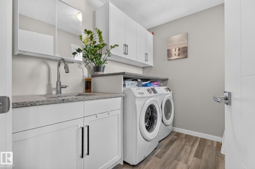 Laundry room featuring wood-finish flooring, white cabinetry, granite-style countertops, and a stainless steel sink with a high-arc faucet - 2534 Wonnacott Loop, Edmonton, AB 