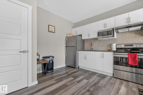 Modern kitchen featuring white cabinetry, stainless steel appliances, and wood-finish flooring - 2534 Wonnacott Loop, Edmonton, AB 