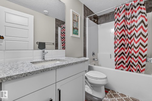 Bathroom featuring a white vanity with a light granite-finish countertop, undermount sink, and chrome faucet - 2534 Wonnacott Loop, Edmonton, AB 