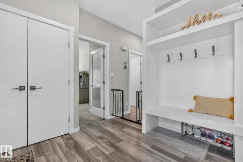 Entryway with wood-finish flooring, built-in white storage bench with hooks, two white panel doors, and a frosted glass-paneled interior door - 2534 Wonnacott Loop, Edmonton, AB 