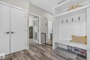 Entryway with wood-finish flooring, built-in white storage bench with hooks, two white panel doors, and a frosted glass-paneled interior door - 2534 Wonnacott Loop, Edmonton, AB 