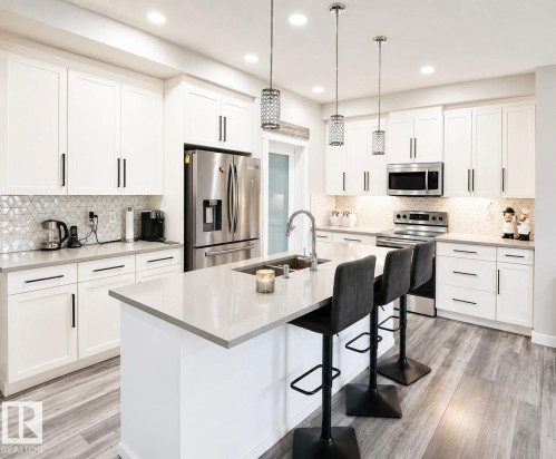 Modern kitchen featuring white shaker cabinetry with black hardware, stainless steel appliances, a hexagonal tile backsplash, light gray countertops, and wood-finish flooring - 2534 Wonnacott Loop, Edmonton, AB 