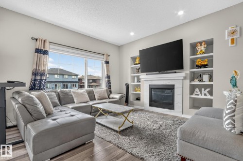 Living area featuring a fireplace with a white surround, built-in shelving, wood-finish flooring, and recessed lighting - 2534 Wonnacott Loop, Edmonton, AB 
