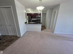 Open-concept living space featuring light-colored carpeting and a partial wall separating the kitchen - 
