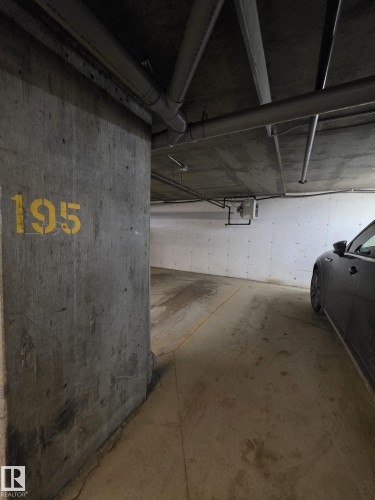 Concrete parking stall with exposed ceiling pipes and overhead lighting - #206 12045 22 Av Sw, Edmonton, AB - Indoor Photo Showing Garage