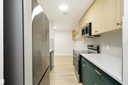 Modern galley kitchen featuring stainless steel appliances, light wood-finish flooring, white countertops, and a textured subway tile backsplash - 18217 84 Avenue Nw, Edmonton, AB 