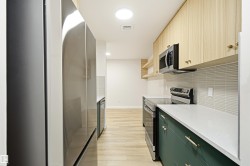 Modern galley kitchen featuring stainless steel appliances, light wood-finish flooring, white countertops, and a textured subway tile backsplash - 