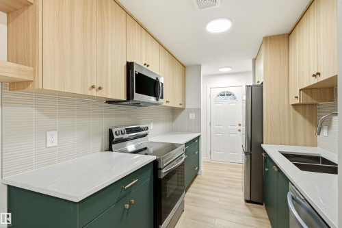 Contemporary kitchen featuring two-tone cabinetry, stainless steel appliances, light-colored countertops, and wood-finish flooring - 18217 84 Avenue Nw, Edmonton, AB 
