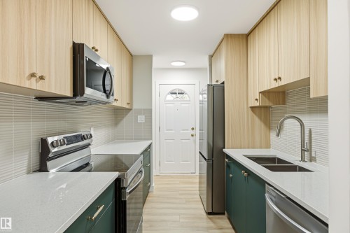 Galley kitchen featuring light wood-finish upper cabinetry, dark green lower cabinetry, and light-colored countertops - 18217 84 Avenue Nw, Edmonton, AB 