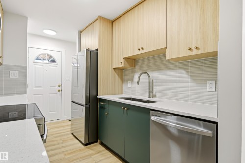 Contemporary kitchen featuring two-tone cabinetry, stainless steel appliances, a double basin sink with a gooseneck faucet, light wood-finish flooring, and a textured tile backsplash - 18217 84 Avenue Nw, Edmonton, AB 