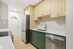 Contemporary kitchen featuring two-tone cabinetry, stainless steel appliances, a double basin sink with a gooseneck faucet, light wood-finish flooring, and a textured tile backsplash - 