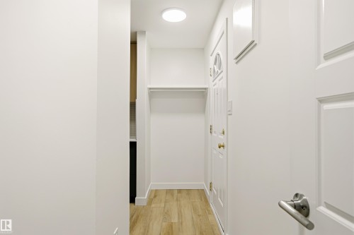 Foyer featuring light wood-finish flooring, a built-in coat rack with shelving, a white paneled front door with decorative glass, and a flush-mount ceiling light - 18217 84 Avenue Nw, Edmonton, AB 