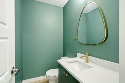 Powder room featuring a sleek vanity with an integrated sink, a white stone-finish countertop, and a modern gold-toned faucet - 