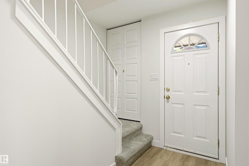 Entryway featuring a paneled door with an arched transom window, wood-finish flooring, a carpeted staircase with a white railing, and a bi-fold closet door - 18217 84 Avenue Nw, Edmonton, AB 