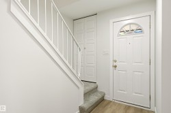 Entryway featuring a paneled door with an arched transom window, wood-finish flooring, a carpeted staircase with a white railing, and a bi-fold closet door - 