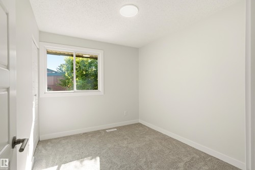 Carpeted room featuring a white interior door with dark hardware, a window, light-toned walls, and a ceiling-mounted light fixture - 18217 84 Avenue Nw, Edmonton, AB 