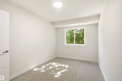 Room featuring a window with green foliage outside, light gray wall paint, gray carpeting, a paneled interior door, and a flush-mount ceiling light fixture - 