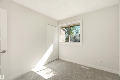 Neutral-toned room featuring a window with white trim, gray carpet flooring, and a paneled bifold closet door - 18217 84 Avenue Nw, Edmonton, AB 