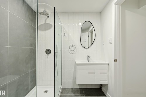 Contemporary bathroom featuring a frameless glass shower enclosure, a rainfall showerhead, and a wall-mounted vanity with integrated sink - 18217 84 Avenue Nw, Edmonton, AB 