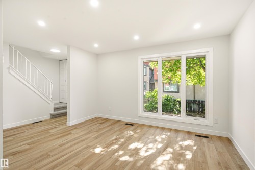 Bright living space featuring wood-finish flooring, recessed lighting, and a large multi-pane window - 18217 84 Avenue Nw, Edmonton, AB 