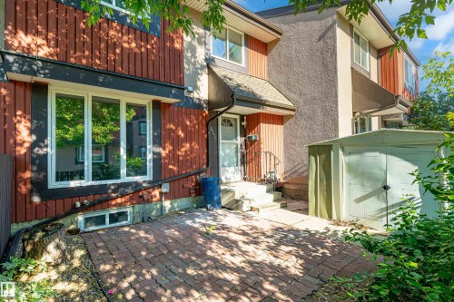 Exterior featuring red vertical panel siding, a stucco finish, multiple white-framed windows, and a paved brick patio - 18217 84 Avenue Nw, Edmonton, AB 