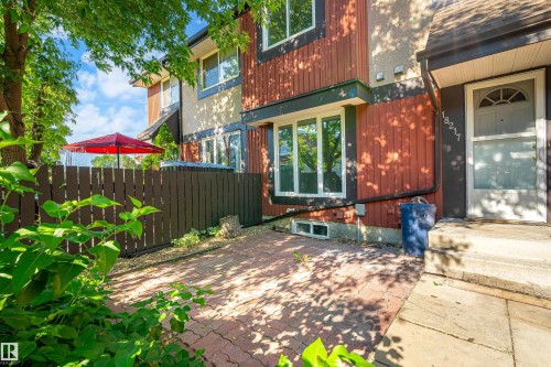 Exterior features include a private patio with brick pavers, a dark wood fence, and mature trees providing natural shade - 18217 84 Avenue Nw, Edmonton, AB 