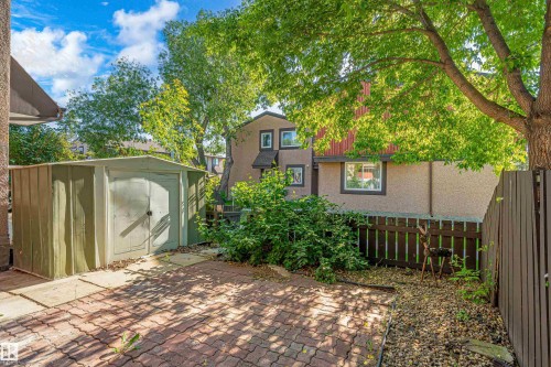 Brick paver patio area featuring a metal storage shed, mature trees, and privacy fencing - 18217 84 Avenue Nw, Edmonton, AB 