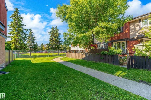 Landscaped common area featuring a curved concrete walkway, expansive green lawn, and mature trees - 18217 84 Avenue Nw, Edmonton, AB 