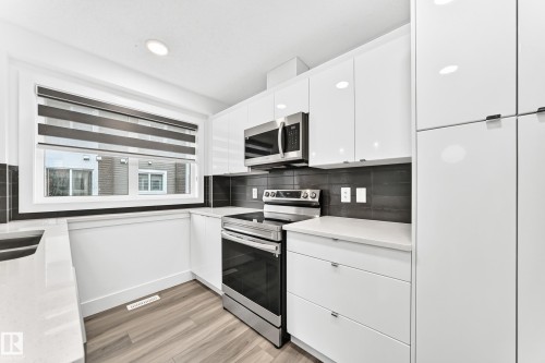Modern kitchen featuring sleek white cabinetry, stainless steel appliances, a dark tile backsplash, light wood-finish flooring, and white countertops - 17 4137 76 Street, Edmonton, AB 