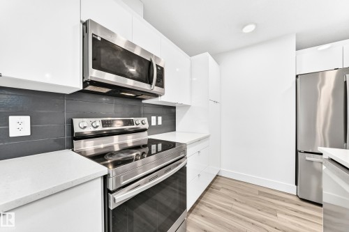 Modern kitchen featuring white cabinetry, stainless steel appliances, light-toned countertops, and a dark tile backsplash - 17 4137 76 Street, Edmonton, AB 
