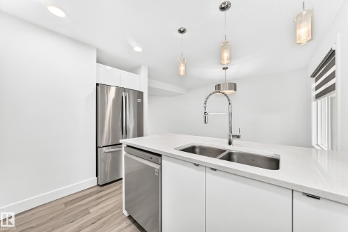 Kitchen island featuring a double basin stainless steel sink with a high-arc faucet, white countertop, and integrated dishwasher - 17 4137 76 Street, Edmonton, AB 