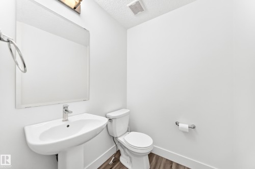 Contemporary powder room featuring a pedestal sink, chrome faucet, rectangular mirror, and wood-finish flooring - 17 4137 76 Street, Edmonton, AB 