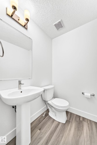 Pedestal sink with chrome faucet, complemented by a white toilet and wood-finish flooring - 17 4137 76 Street, Edmonton, AB 