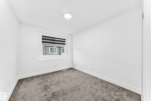 Neutral-toned room featuring a single window with blinds, overhead flush-mount lighting, clean white walls, wide baseboards, and soft carpet flooring - 17 4137 76 Street, Edmonton, AB 