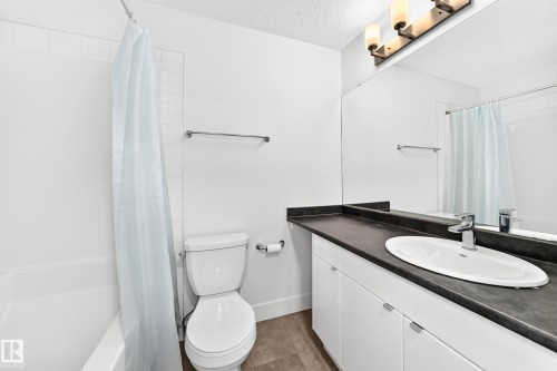 Bathroom featuring an integrated bathtub and shower, white subway tile surround, single vanity with dark countertop, white cabinetry, and wall-mounted mirror - 17 4137 76 Street, Edmonton, AB 