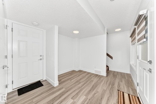 Entryway featuring wood-finish flooring, recessed lighting, white panel doors, and a window with roller shades - 17 4137 76 Street, Edmonton, AB 