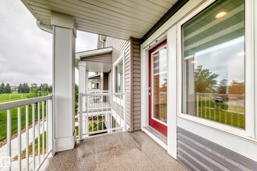 Private balcony with textured concrete flooring, white metal railings, and an opaque red entry door - 17 4137 76 Street, Edmonton, AB 