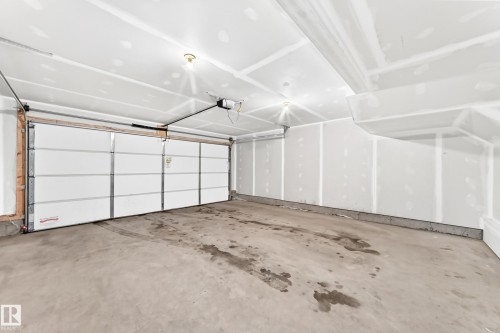 Spacious garage with a white panel garage door, automatic opener, drywall-finished walls, and a concrete floor - 17 4137 76 Street, Edmonton, AB 